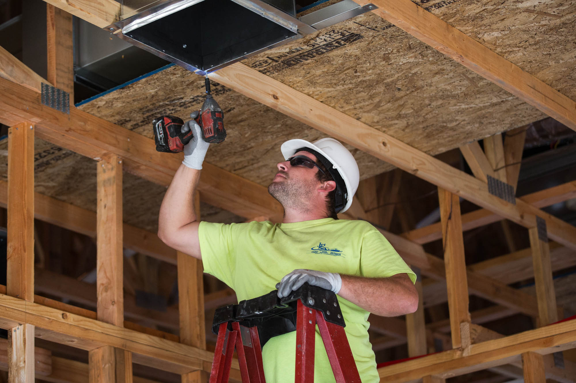 A man installing duct work on a ceiling